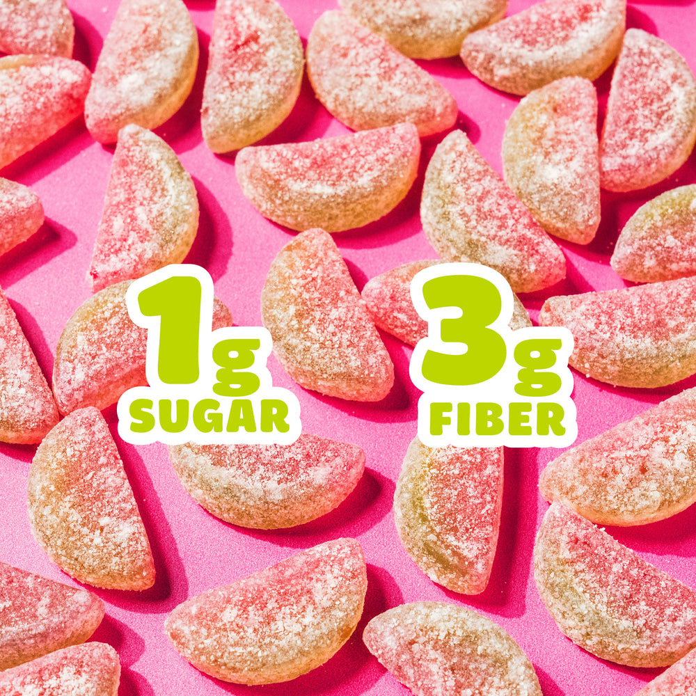 Pile of sour watermelon gummy candies on a pink background with large text overlays reading "1g SUGAR" and "3g FIBER".