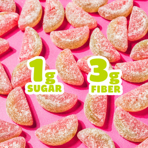 Pile of sour watermelon gummy candies on a pink background with large text overlays reading "1g SUGAR" and "3g FIBER".