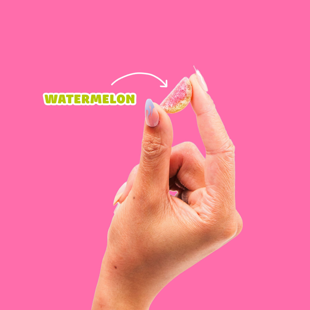 Hand holding a sour watermelon gummy candy on a pink background with an arrow pointing from the word "WATERMELON".
