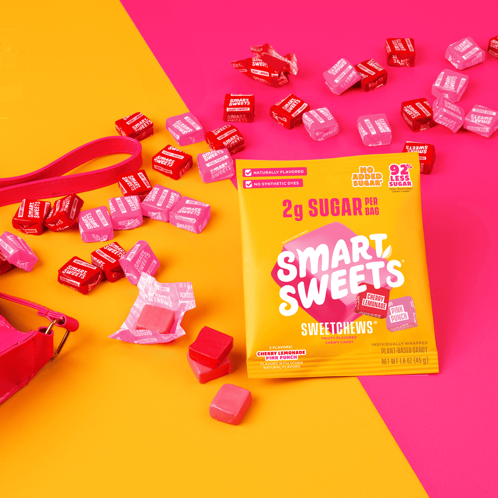 SweetChews bag on a yellow and pink background, surrounded by scattered pink and red unwrapped and individually wrapped chewy candies.