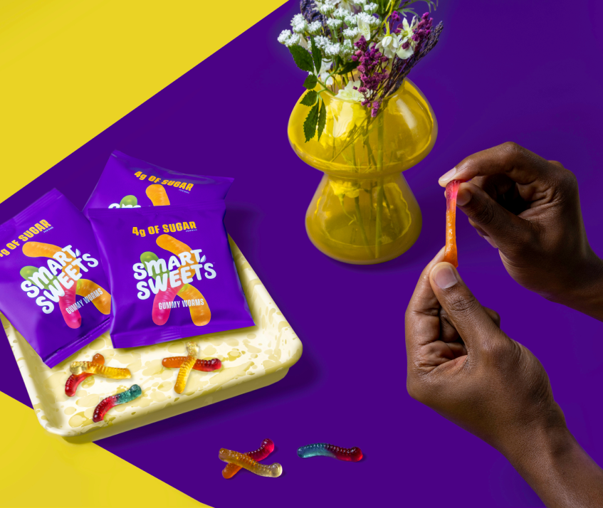 Gummy Worms pouches on tray and someone holding a gummy worm